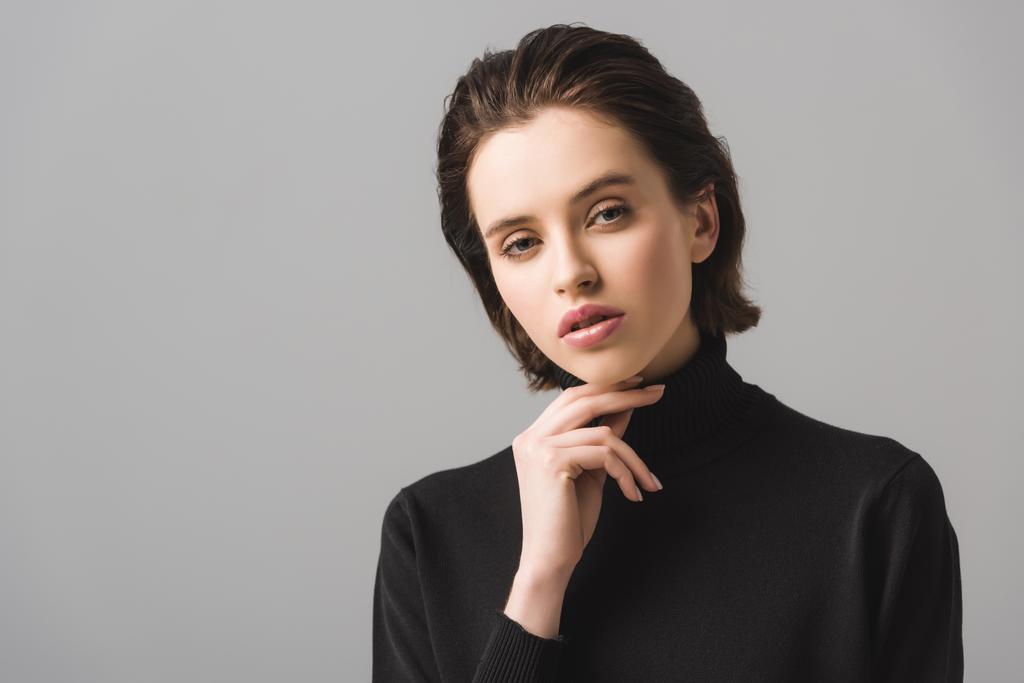 pensive young woman in black jumper looking at camera isolated on grey  - Photo, Image