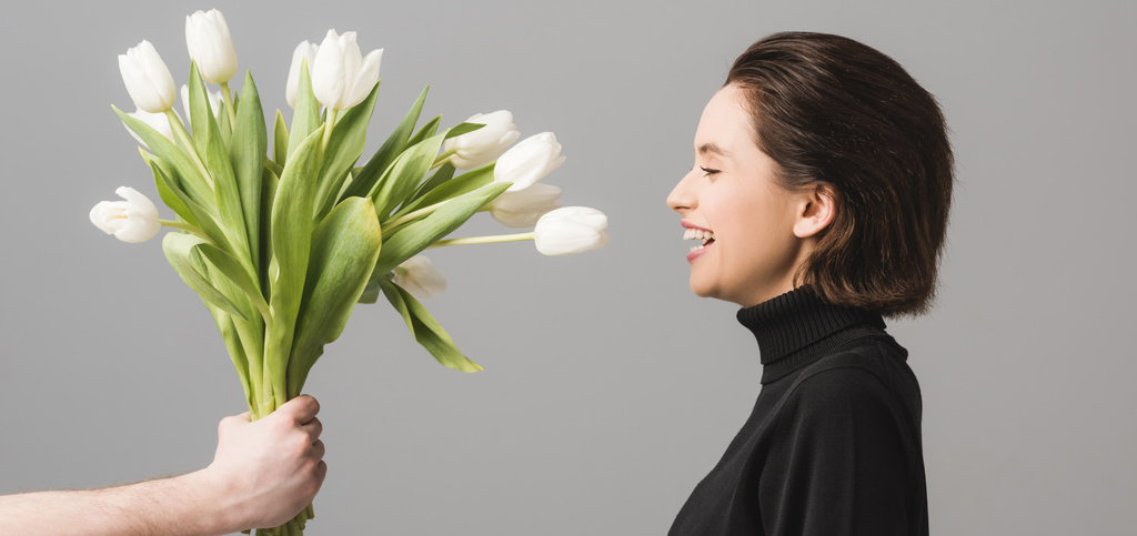 colpo panoramico di uomo che tiene tulipani bianchi vicino a donna allegra isolata su grigio
  - Foto, immagini
