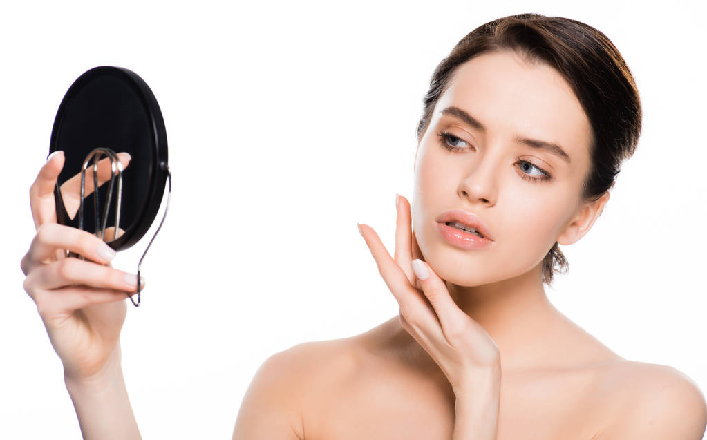 young brunette woman touching face and looking at mirror isolated on white  - Photo, Image