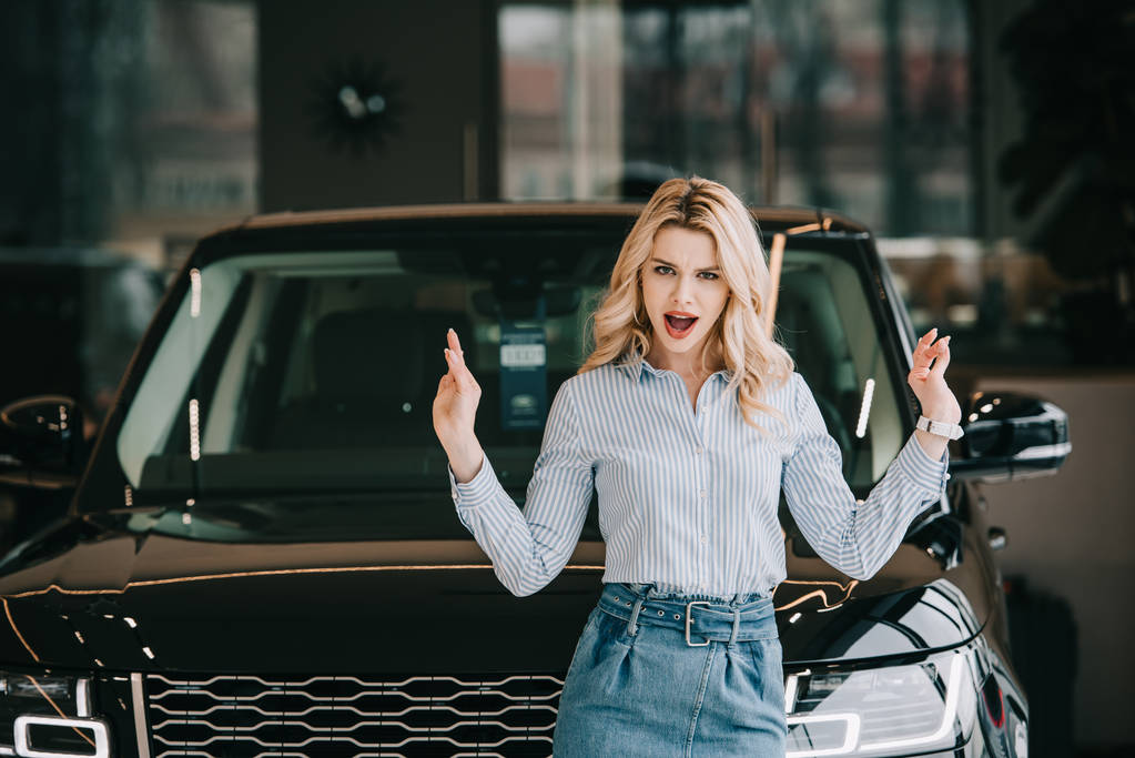 attractive blonde girl screaming and gesturing near black car  - Photo, Image