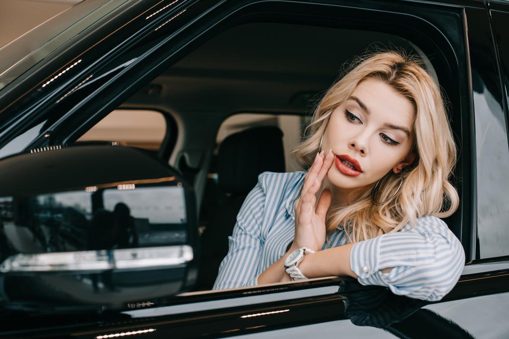 ελκυστική ξανθιά κορίτσι κοιτάζοντας καθρέφτη του αυτοκινήτου, ενώ αγγίζοντας το πρόσωπο  - Φωτογραφία, εικόνα