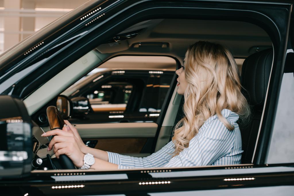 attraktive blonde Frau am Steuer, während sie im Auto sitzt  - Foto, Bild