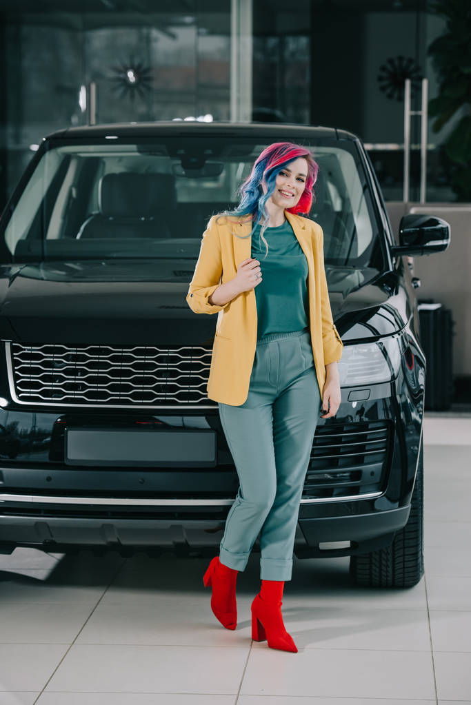 wesoły dziewczyna z kolorowymi włosami stoi w pobliżu czarnego samochodu  - Zdjęcie, obraz