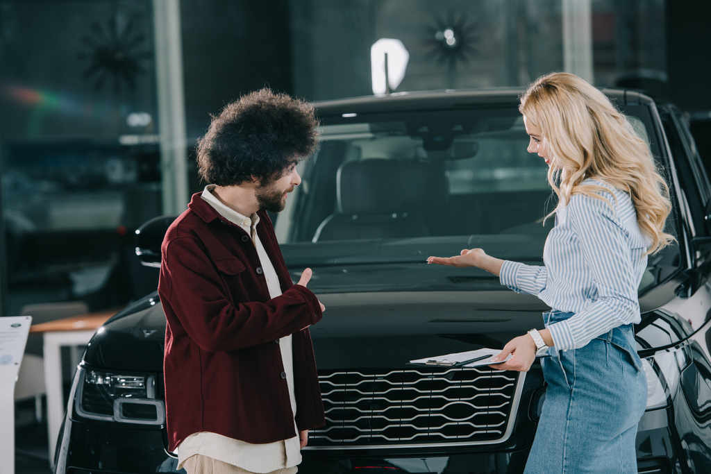 blonde car dealer showing black automobile to curly man  - Photo, Image