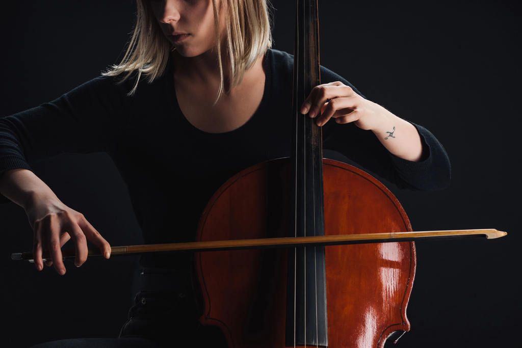обрізаний вид татуйованої жінки, що грає подвійний бас у темряві ізольовано на чорному
 - Фото, зображення
