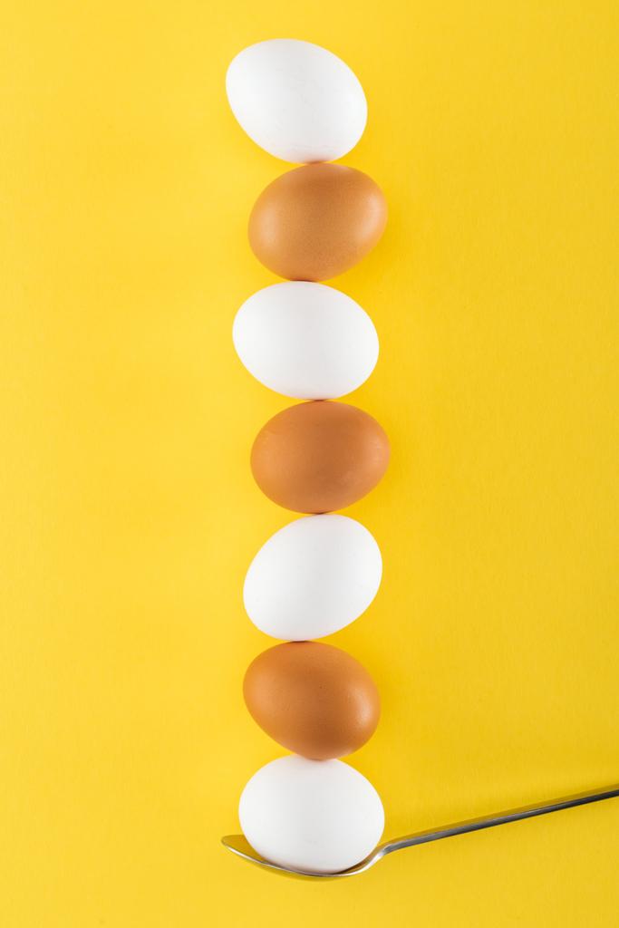 επτά λευκά και καφέ αυγά κοτόπουλου σε κουτάλι σε κίτρινο φόντο - Φωτογραφία, εικόνα