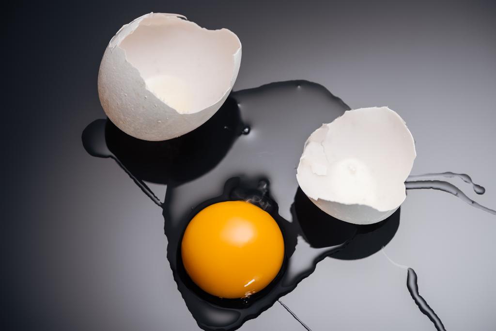 Nahaufnahme von frisch zertrümmertem Hühnerei mit Eigelb, Eiweiß und Eierschale auf schwarzem Hintergrund - Foto, Bild