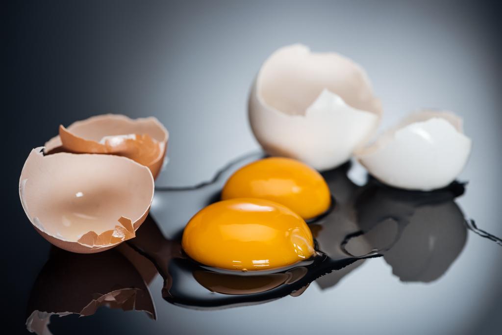 selective focus of raw smashed chicken eggs with yolks, proteins and eggshell on black background - Photo, Image