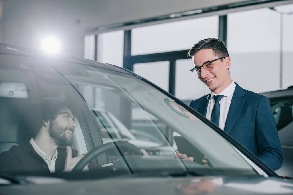 Veselý obchodník s brýlemi, stojící v červeném autě u kudrnatých mužů  - Fotografie, Obrázek
