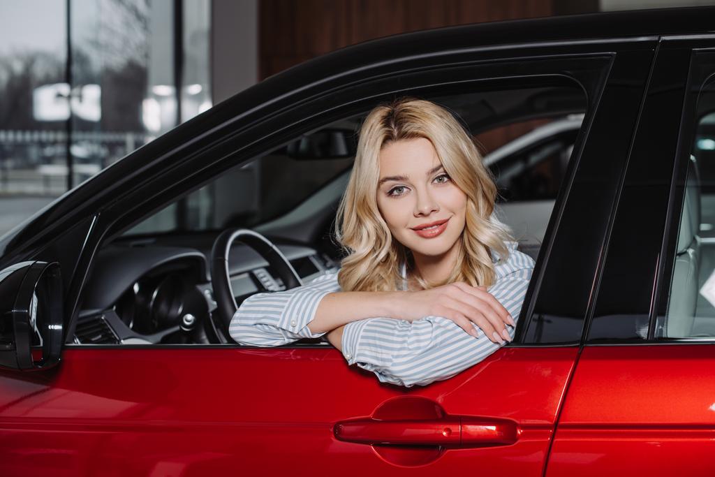 Kırmızı arabada otururken kamera bakarak güzel genç kadın  - Fotoğraf, Görsel