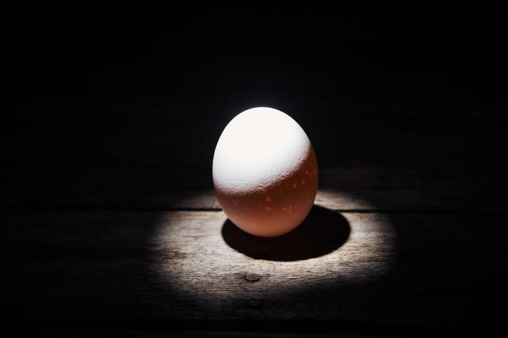 białe jajko z kurczaka w ciemności na wywietrzonej powierzchni drewnianej  - Zdjęcie, obraz
