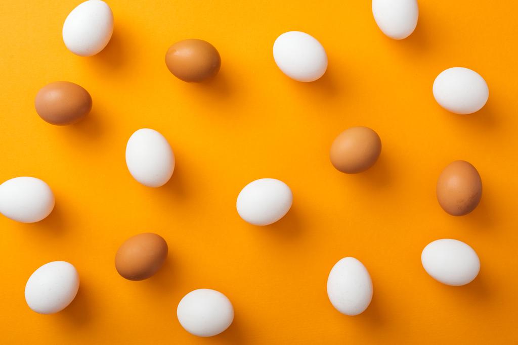 Κορυφαία θέα των ολόκληρων λευκών και καφέ βιολογικών αυγών κοτόπουλου σε φωτεινό πορτοκαλί φόντο  - Φωτογραφία, εικόνα