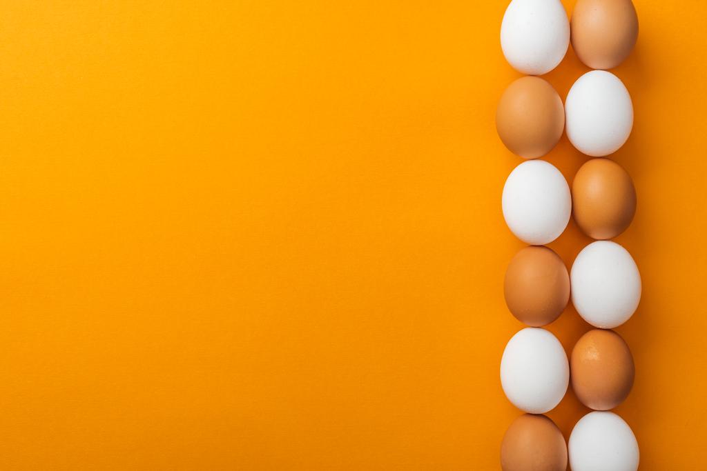 верхний вид белых и коричневых органических куриных яиц на ярко-оранжевом фоне с копировальным местом
 - Фото, изображение