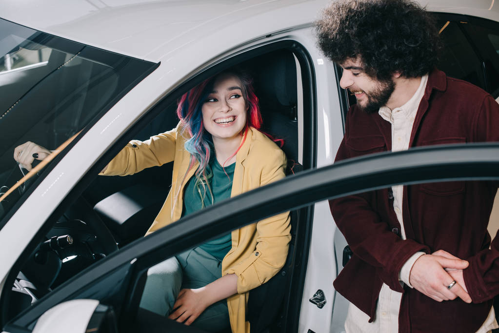 εναέρια όψη του χαρούμενο κορίτσι με χρωματιστά μαλλιά κάθονται στο αυτοκίνητο και κοιτάζοντας σγουρά άνθρωπος  - Φωτογραφία, εικόνα