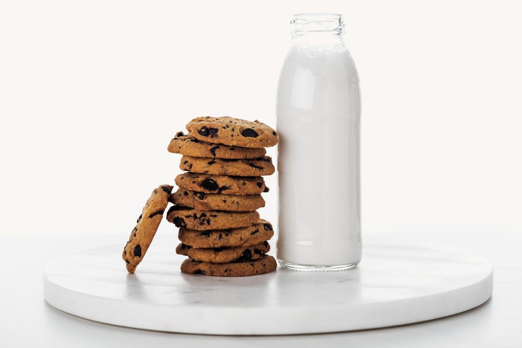 白の上に分離されたミルクとボトルの近くにおいしいチョコレートのクッキーの山 - 写真・画像
