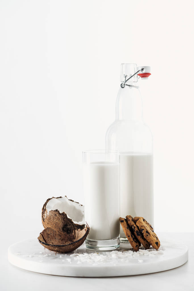 Kokosnuss vegane Milch in Glas und Flasche in der Nähe von Kokosnuss und Schokoladenkeksen isoliert auf weiß - Foto, Bild