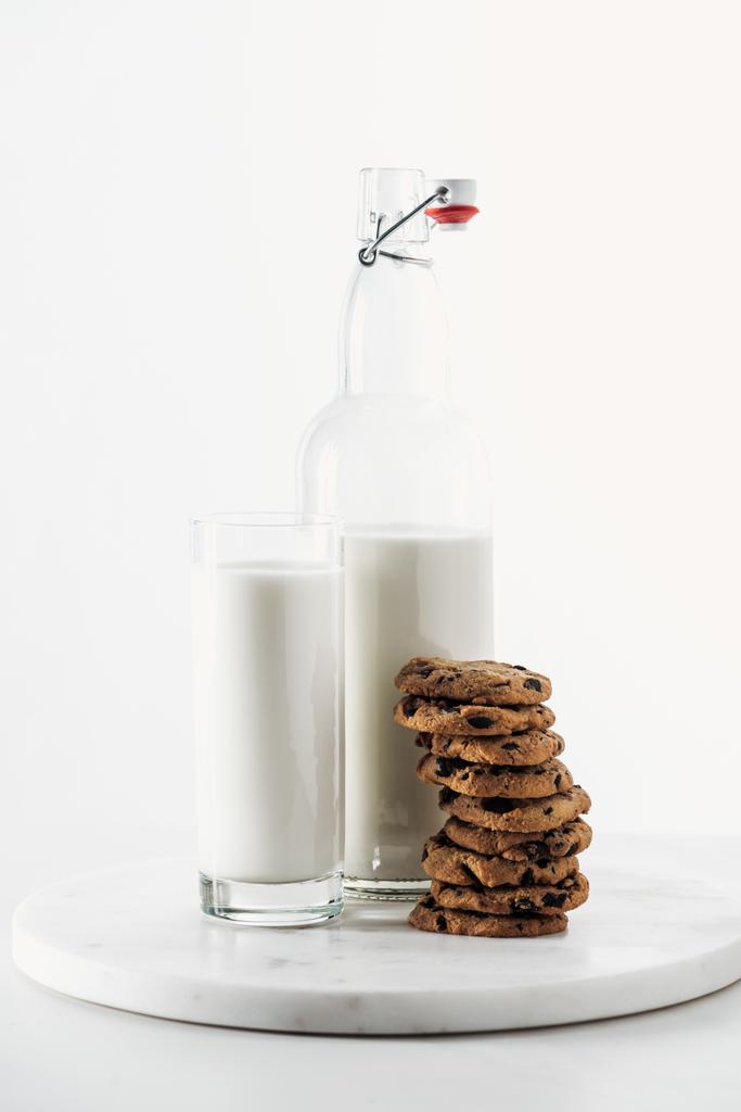 白の上に孤立した新鮮なミルクとボトルとガラスの近くにおいしいチョコレートのクッキーの山 - 写真・画像