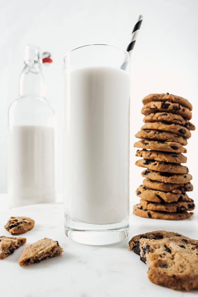 チョコレートクッキーと大理石テーブルのボトルの近くに新鮮な牛乳とわらとガラスの選択的焦点 - 写真・画像