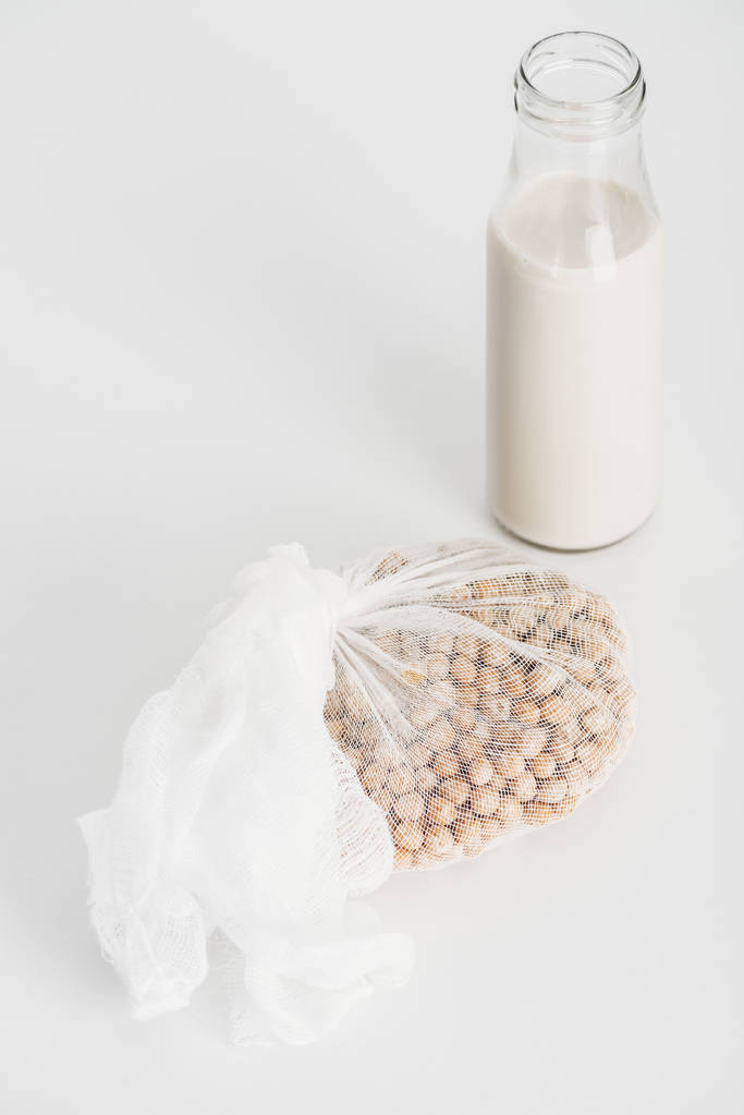 kikkererwten in wit kaasdoek bij fles met veganistische kikkererwten melk op grijze achtergrond - Foto, afbeelding