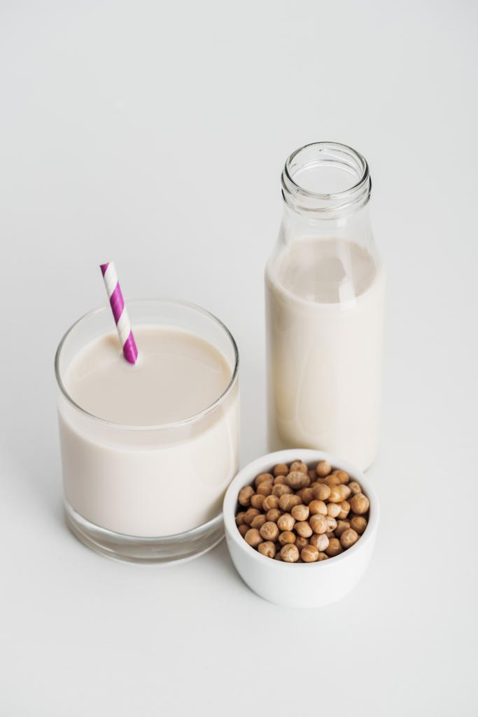 kikkererwten in kom in de buurt van fles en glas met veganistische kikkererwten melk op grijze achtergrond - Foto, afbeelding