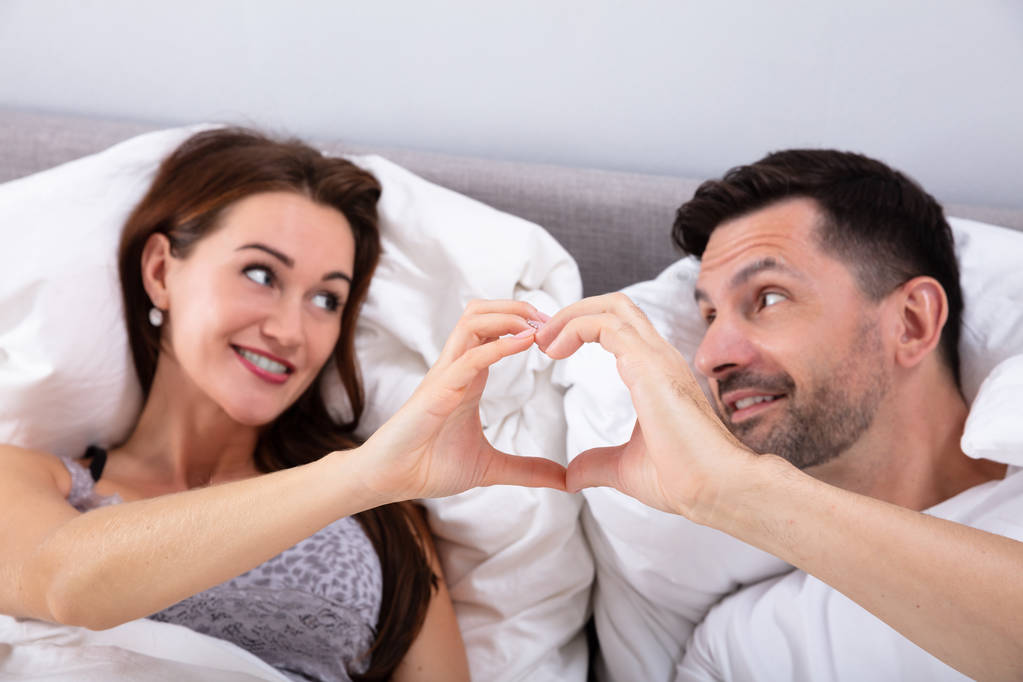 glückliches Paar liegt auf Bett und macht Herzform - Foto, Bild