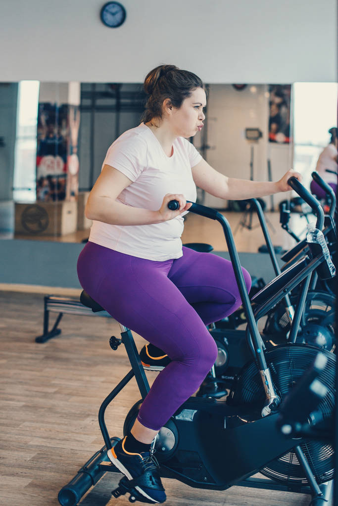 Lihava nainen voimakkaasti käyttäessään paikallaan pyörä
 - Valokuva, kuva