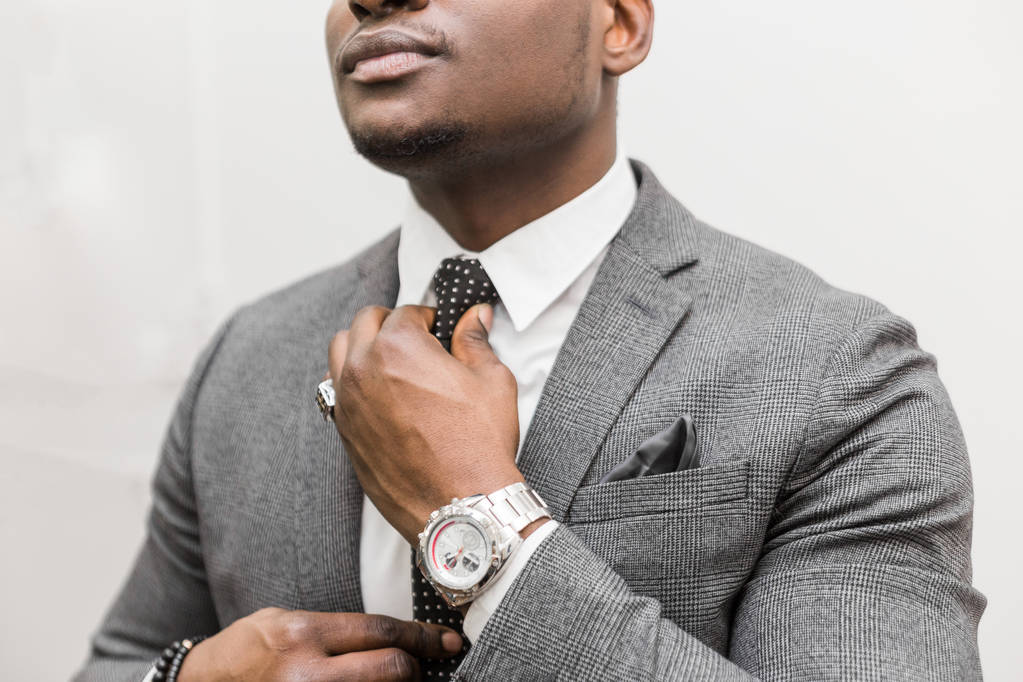 Mladý africký americký podnikatel v šedém obleku vázací kravata na bílém pozadí. - Fotografie, Obrázek