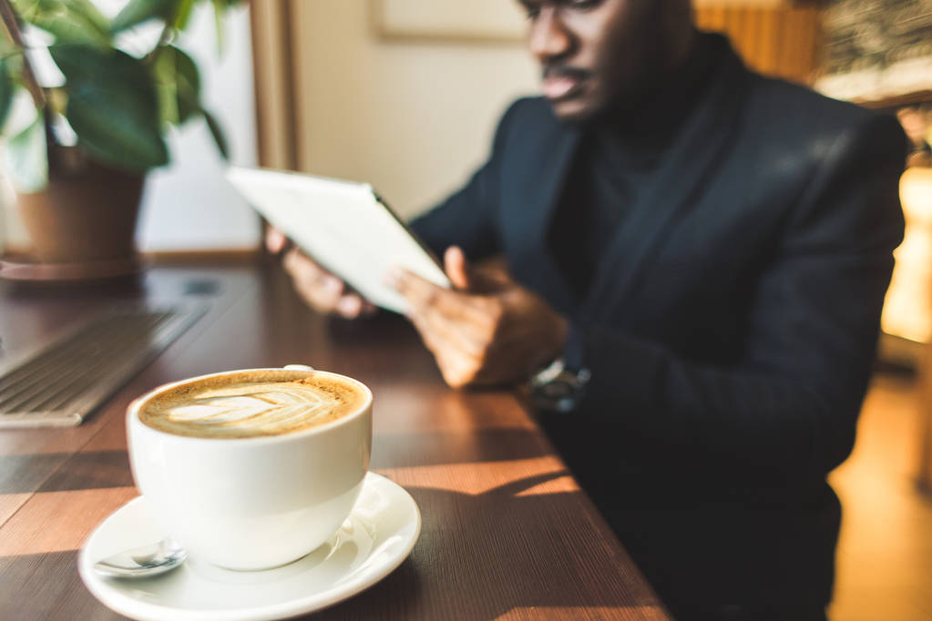 Jeune homme d'affaires à la peau foncée avec tablette dans un café avec une tasse de café
. - Photo, image