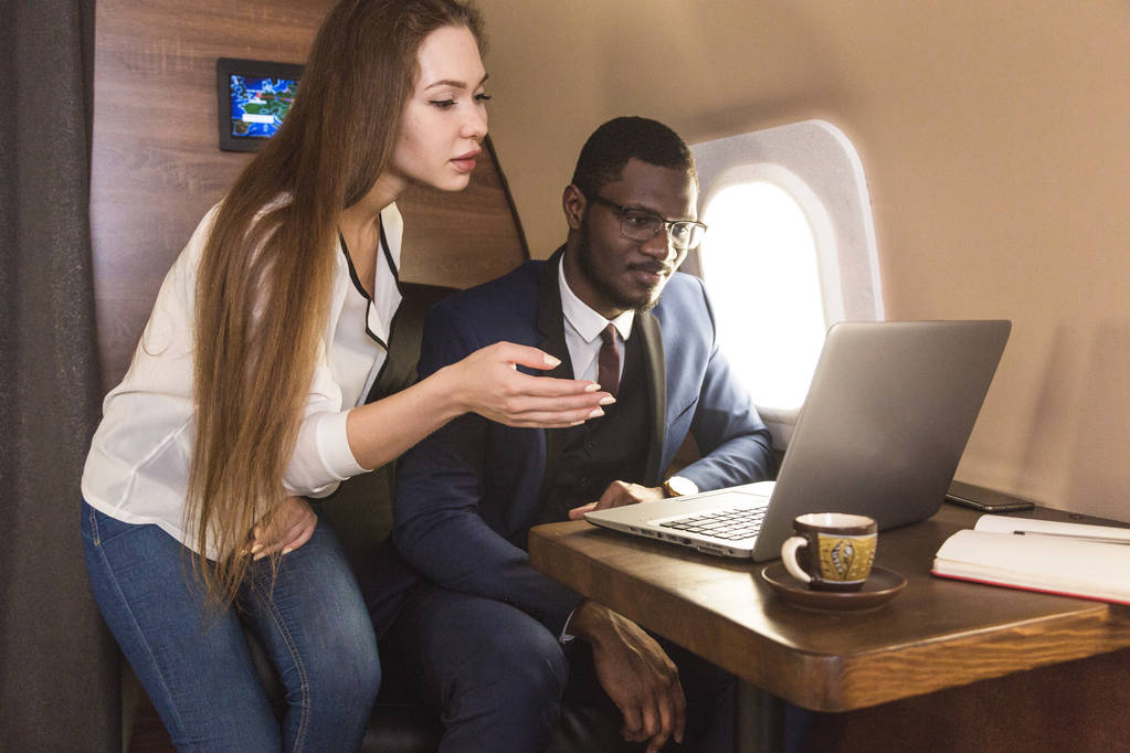 Young successful African-American businessman with glasses and an attractive female workmate blonde in a private jet. Service and flight first class - Photo, Image