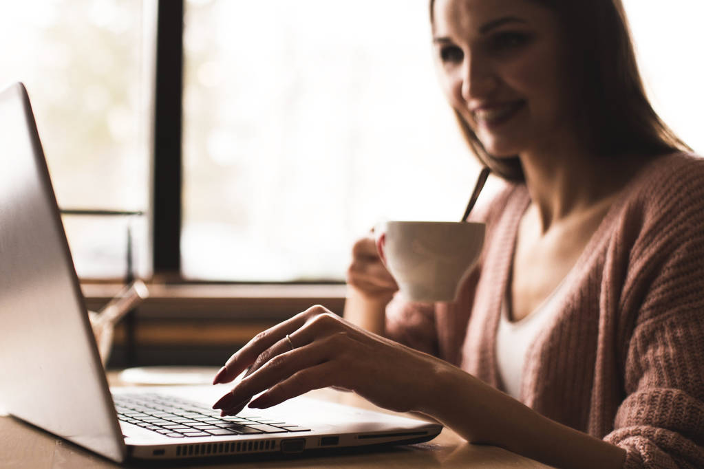 Houkutteleva nuori nainen istuu pöydän ääressä kahvilassa kupin kahvia ja nauttii kannettava tietokone - Valokuva, kuva