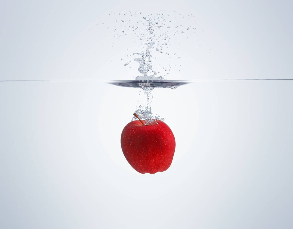 Apfel fällt ins Wasser und verteilt viele Spritzer und Tropfen - Foto, Bild