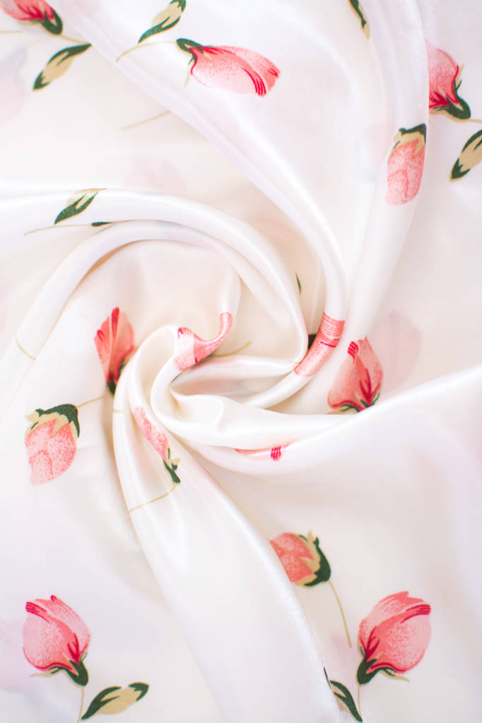 Jedwabna pomarszczona biała tkanina z różowymi kwiatami. Widok z góry. Koncepcja tekstyliów i tekstur-zbliżenie jedwabistych, białych faliste tło tkaniny - Zdjęcie, obraz