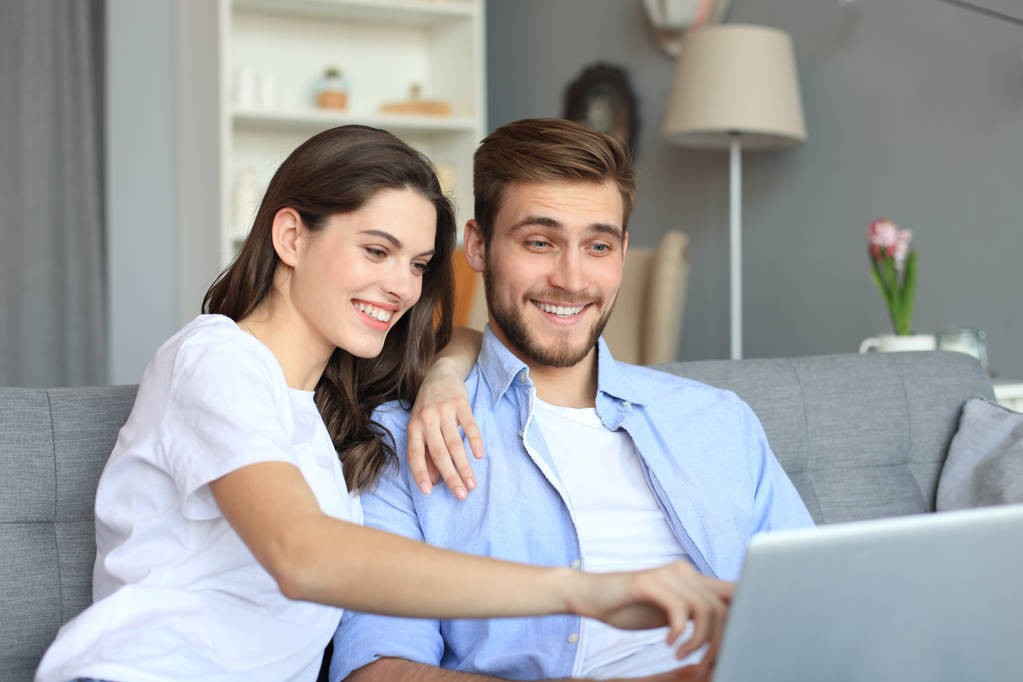 Jeune couple faisant quelques achats en ligne à la maison, en utilisant un ordinateur portable sur le canapé
. - Photo, image