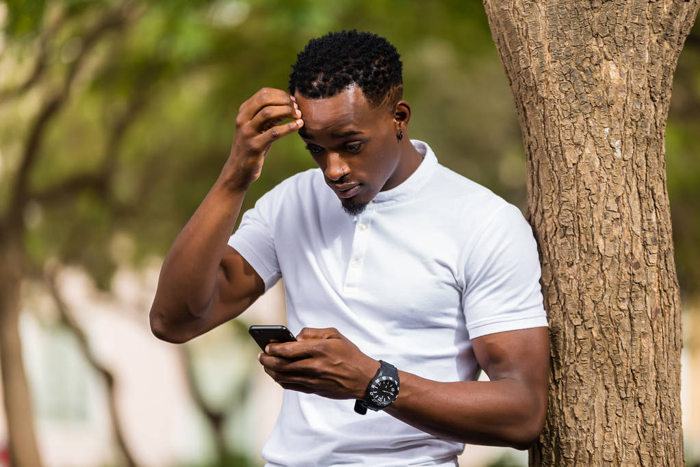 Außenporträt eines jungen schwarzafrikanisch-amerikanischen Mannes beim SMS-Schreiben   - Foto, Bild