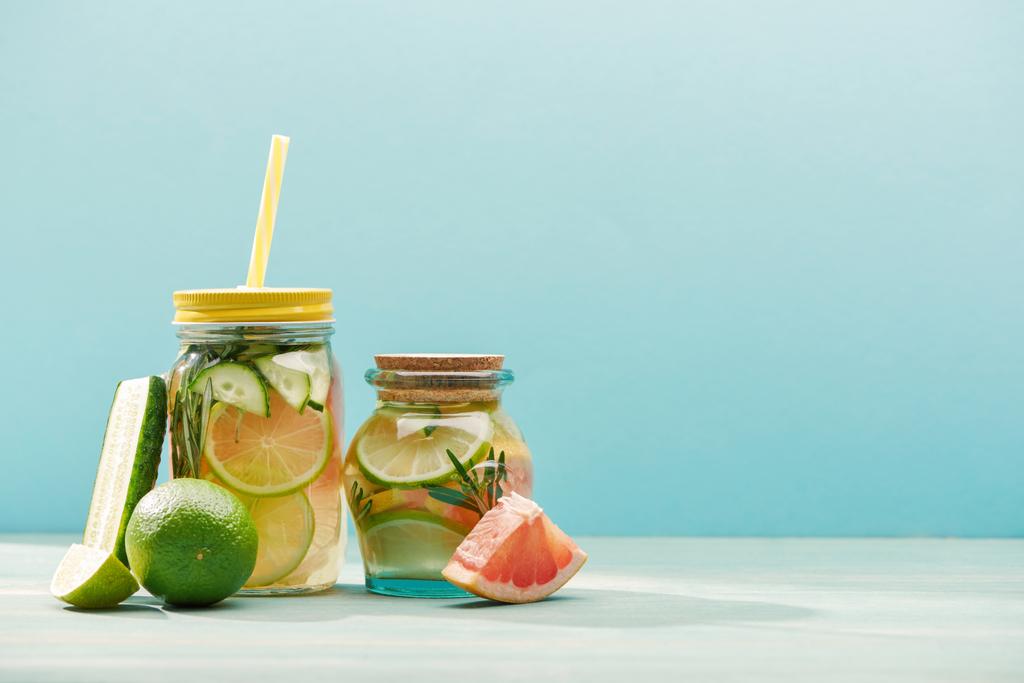 friss méregtelenítő italokat tégelyek közelében lime, uborka és grapefruit izolált kék - Fotó, kép