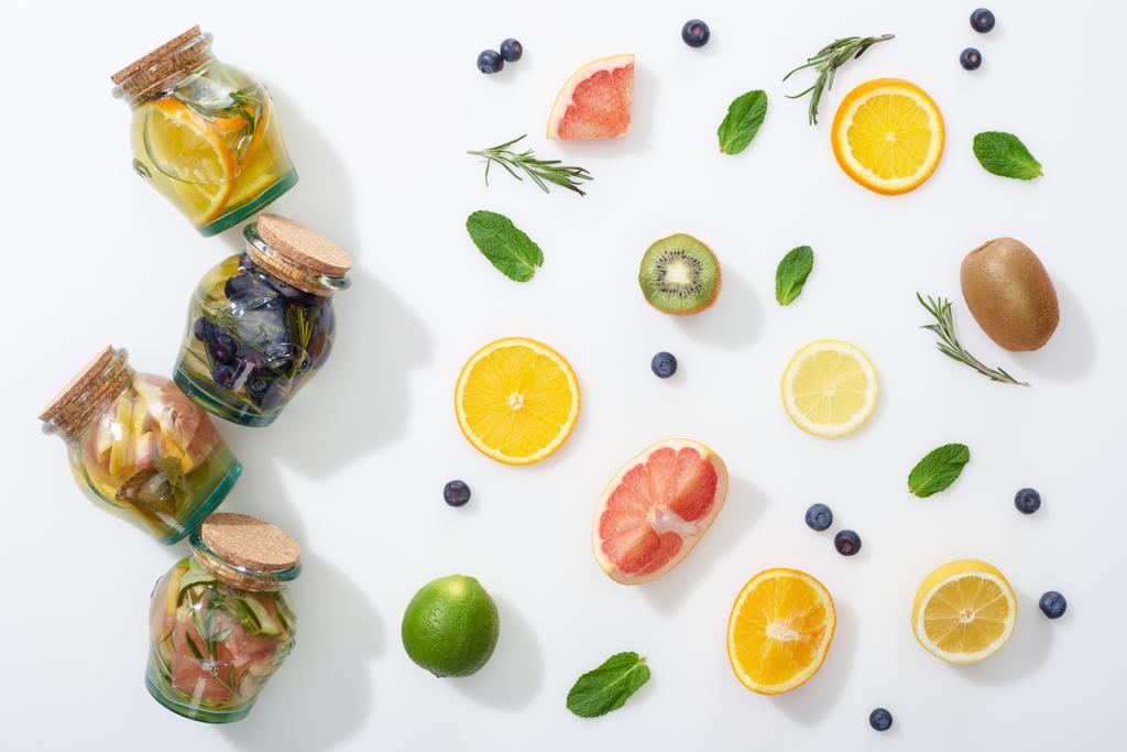 vista dall'alto di bevande disintossicanti in barattoli vicino a fette di frutta, bacche, menta e rosmarino
 - Foto, immagini