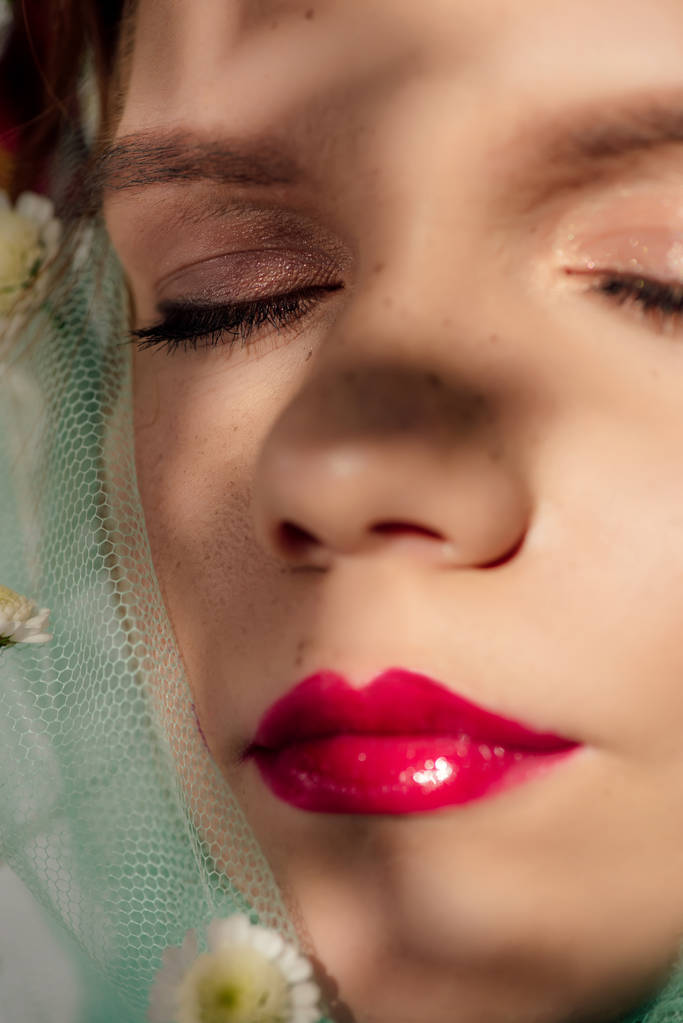 zblízka pohled na krásnou mladou ženu s očima zavřených a červenými rty pokrytou květinami - Fotografie, Obrázek