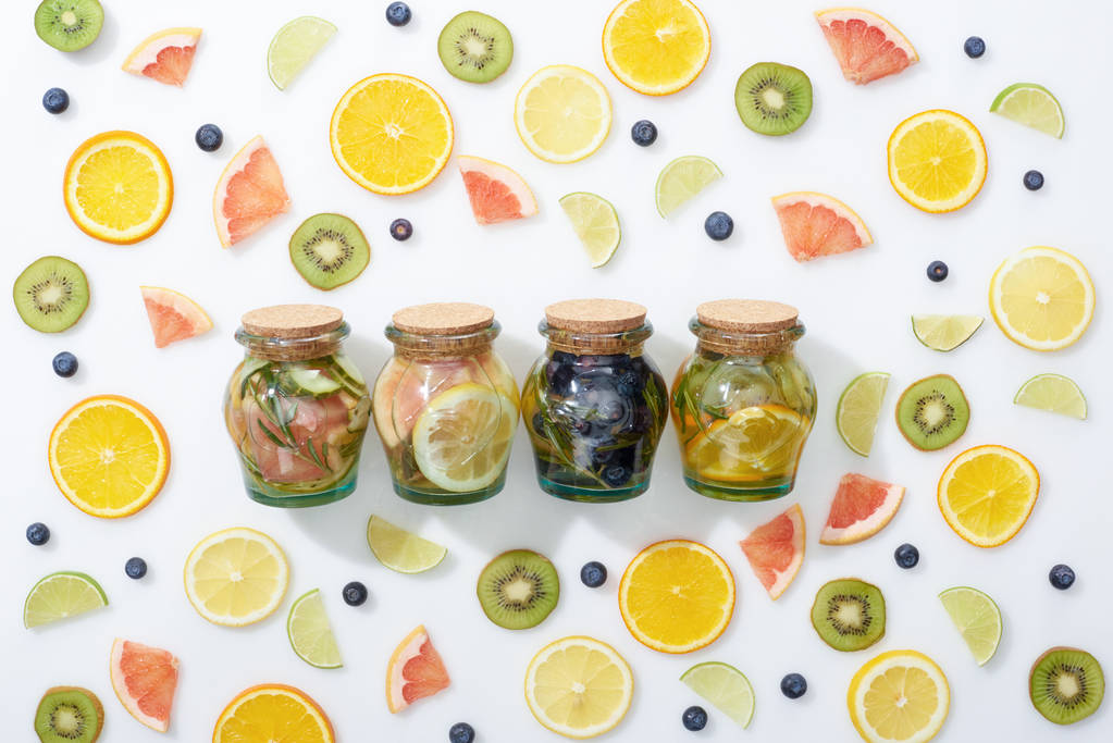 top view of detox drinks in jars among sliced fruits and blueberries on white background - Photo, Image