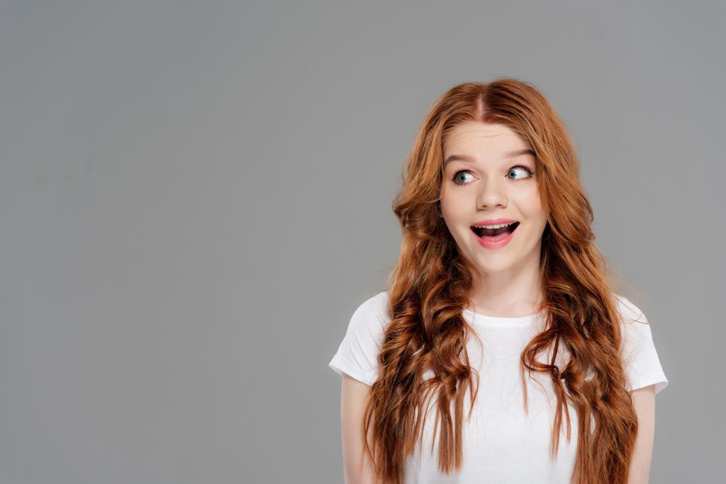 Happy Redhead meisje op zoek weg geïsoleerd op grijs met kopieerruimte - Foto, afbeelding