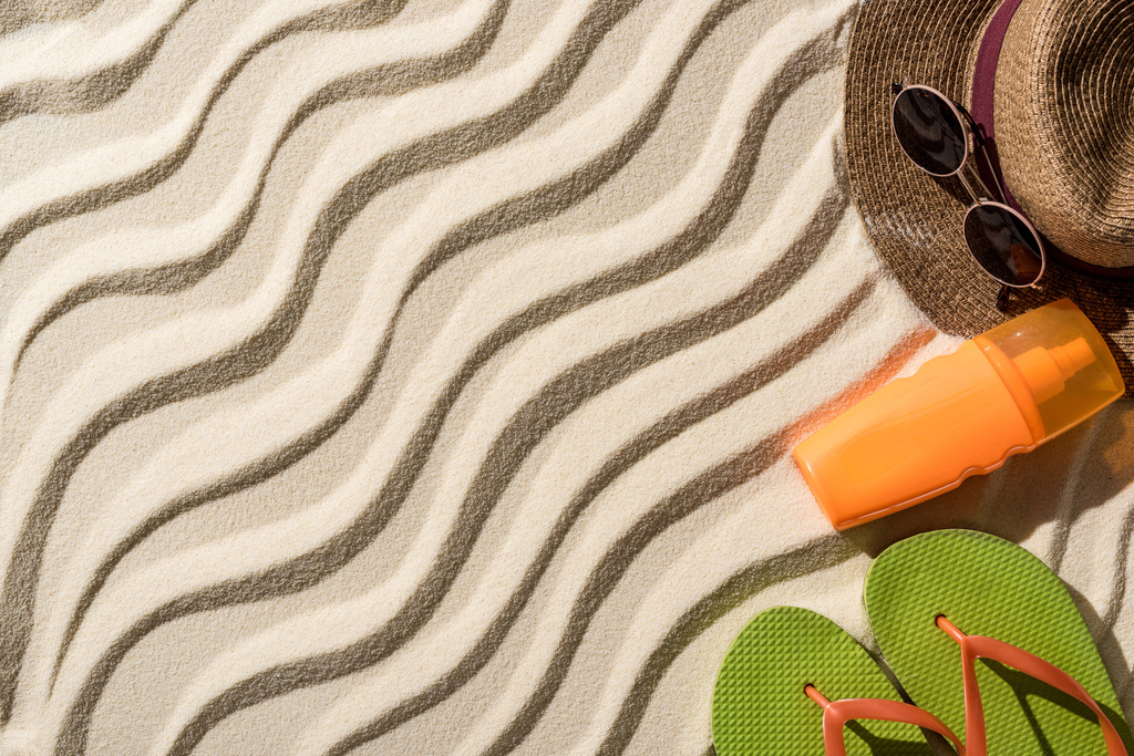 bovenaanzicht van strohoed, flip flops, zonnebrandcrème en zonnebril op golvend zand met kopieerruimte - Foto, afbeelding