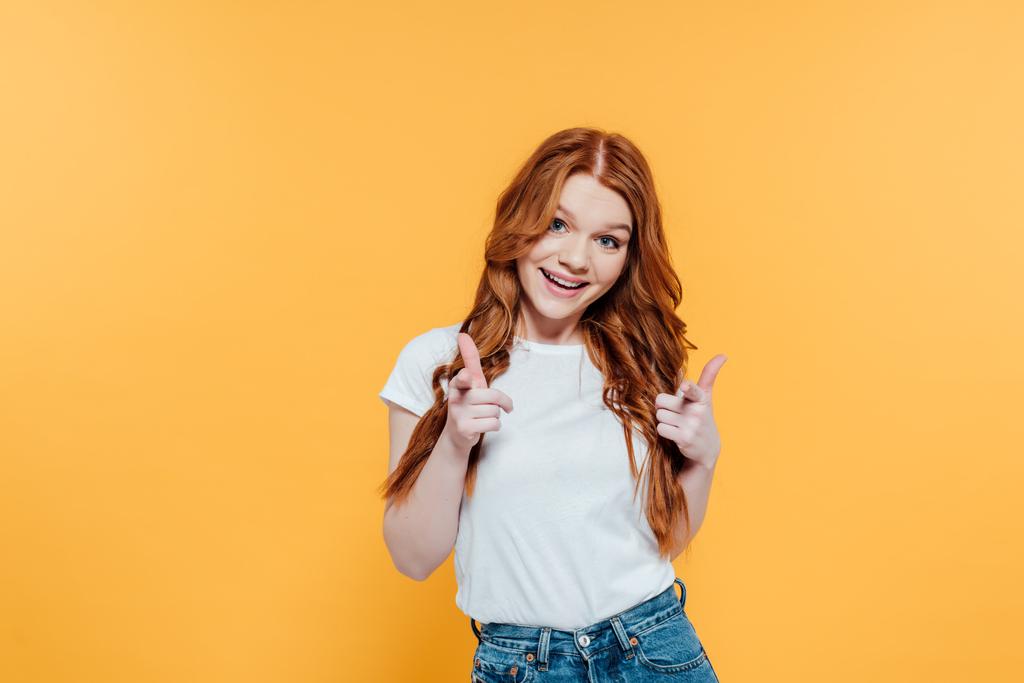beautiful smiling redhead girl pointing with fingers at camera isolated on yellow - Photo, Image