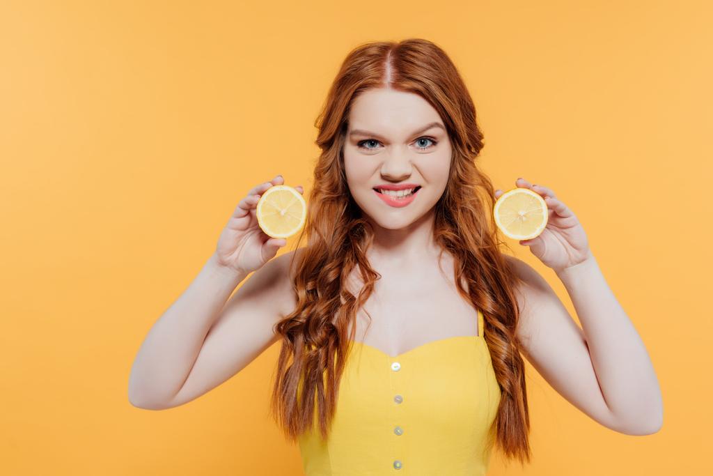 redhead girl holding lemons, looking at camera and making facial expression isolated on yellow - Photo, Image
