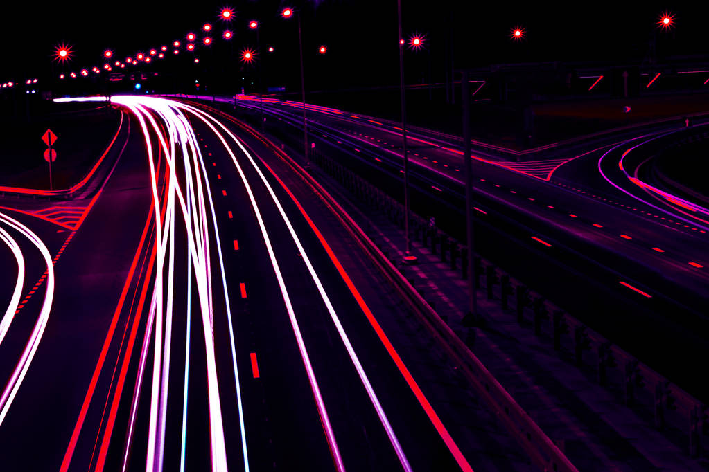 Autók könnyű pályák, íves autópályán éjjel. Éjszakai közlekedési pályák. Elmosódást csökkentse. Éjszakai város közúti forgalom fényszóró mozgás. Városképet gazdagító épületnek szánták. Kigyullad a közúti jármű motion blur által. - Fotó, kép
