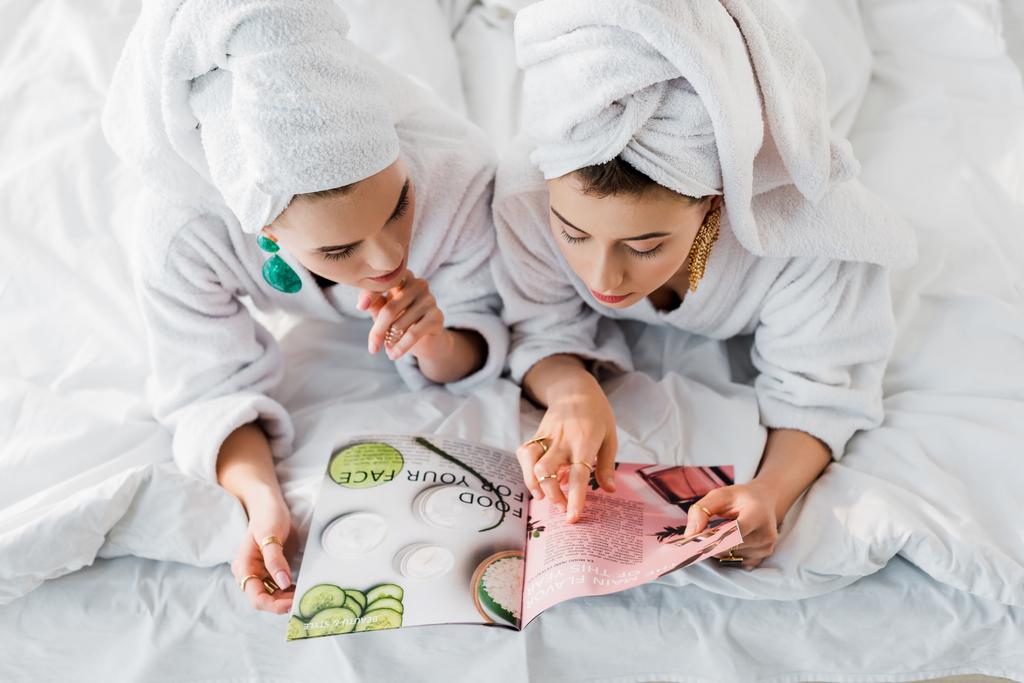 バスローブ、イヤリング、ベッドに横たわっている間に一緒に雑誌を読んで頭の上にタオルでスタイリッシュな女性のオーバーヘッドビュー - 写真・画像