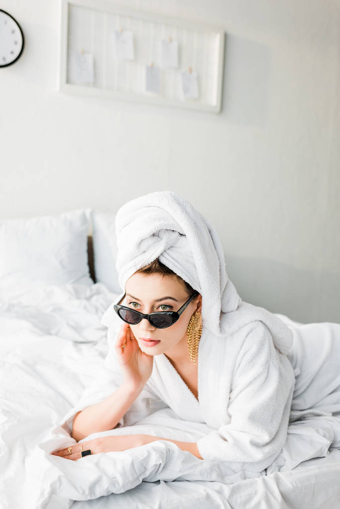 stylish woman in bathrobe and sunglasses, towel and jewelry lying in bed  - Photo, Image