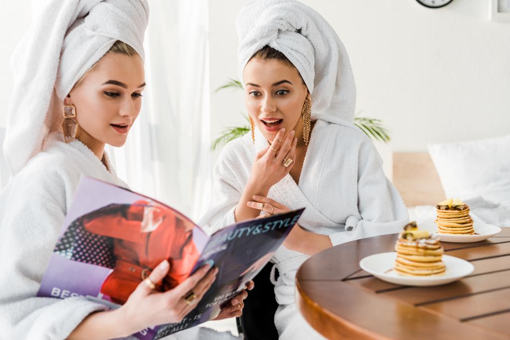 foyer sélectif des femmes élégantes surpris dans les peignoirs et les bijoux avec des serviettes sur les têtes lecture magazine ensemble près de la table avec des crêpes
 - Photo, image