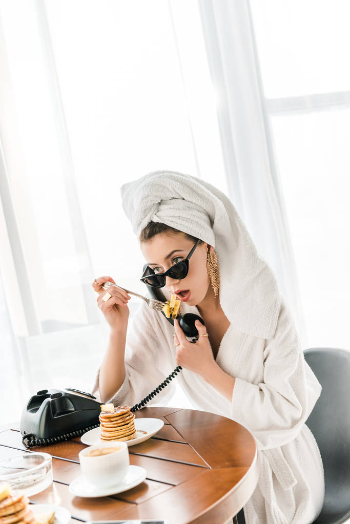 femme élégante en peignoir, lunettes de soleil et bijoux avec serviette sur la tête parler sur le téléphone vintage tout en mangeant des crêpes
 - Photo, image