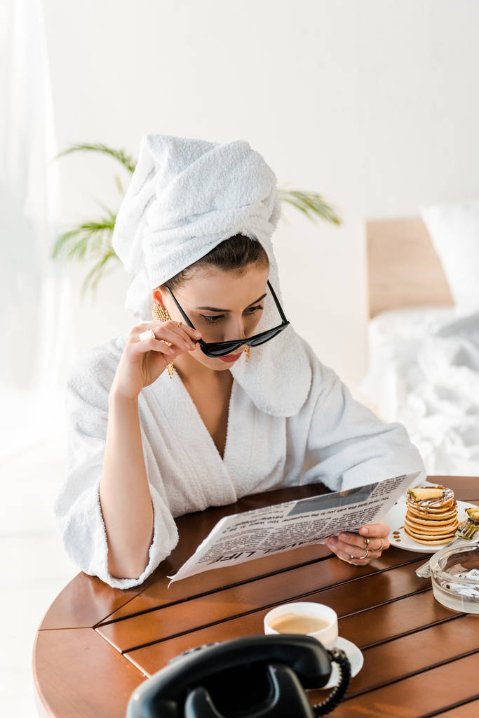 mulher de roupão de banho, óculos de sol e jóias com toalha na cabeça ler jornal de manhã
 - Foto, Imagem