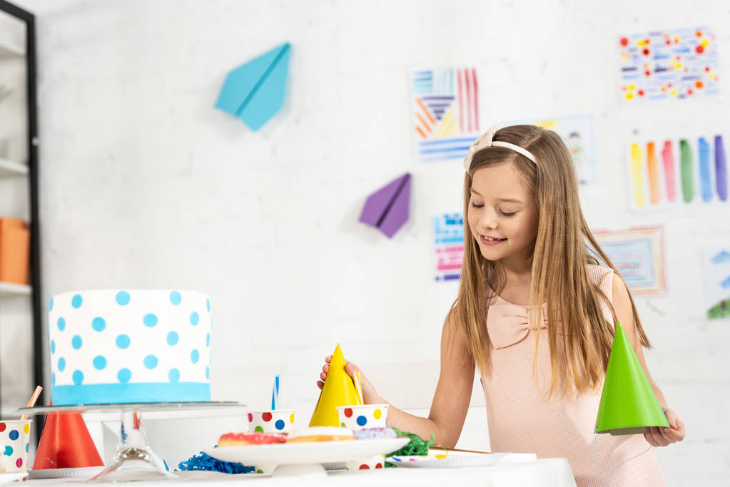 adorable enfant souriant à la table festive avec casquettes de fête et gâteau d'anniversaire
 - Photo, image