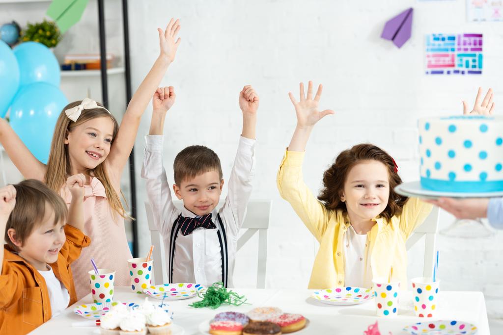 suloiset lapset istuvat pöydässä, hurraavat ja odottavat kakkua syntymäpäiväjuhlien aikana
 - Valokuva, kuva